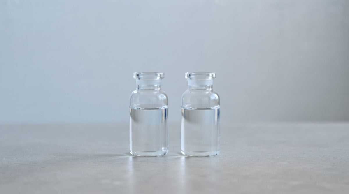 Two clear glass sample vials filled with water, set against a soft blue-grey and neutral background.